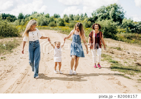 Several generations of women of the same family are walking along a dirt road outside the city, enjoying the time spent together 82008157