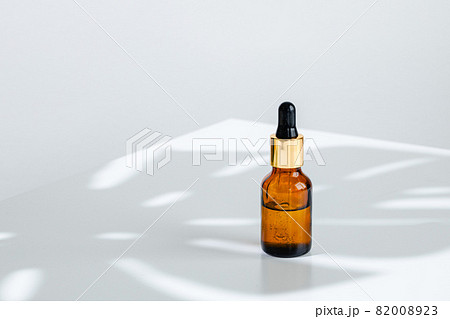 Creative photo of cosmetic bottle with pipette on a white background with shadow of tropical flower 82008923