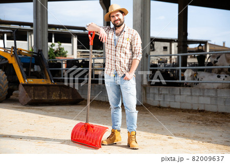Young man farmer with shovel standing near agrimotor Young man farmer with shovel standing near agrimotor 82009637