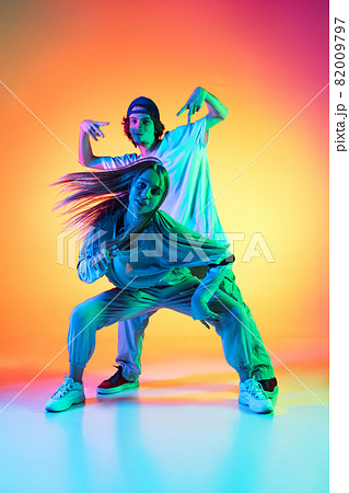 Young hip-hop dancers, stylish emotive girl and boy in action and motion in casual sports youth clothes on gradient multi colored background at dance hall in neon light. 82009797