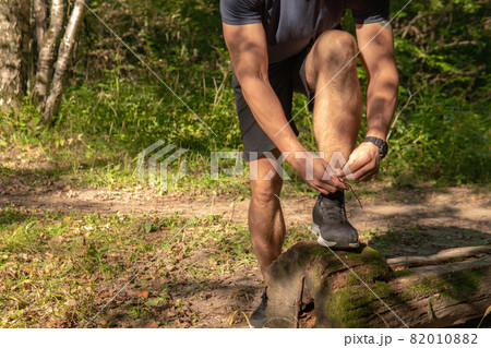 The sportsman is tying the laces of his legs in sneakers close up the athlete runs in the park outdoors, around the forest, oak trees green grass young enduring athletic athlete run athlete fitness 82010882