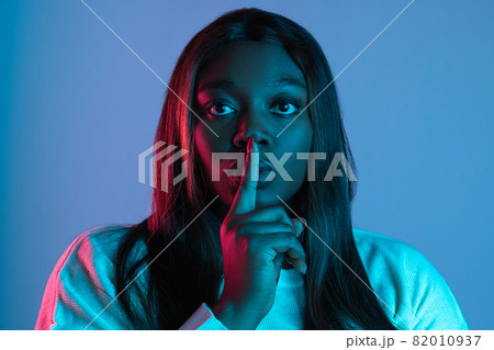 Close-up portrait of African charming woman with long straight hair isolated on blue studio background in neon light. Concept of human emotions Close-up portrait of African charming woman with long straight hair isolated on blue studio background in neon light. Concept of human emotions 82010937
