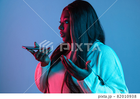 Portrait of African charming woman with long straight hair isolated on blue studio background in neon light. Concept of human emotions. Side view Portrait of African charming woman with long straight hair isolated on blue studio background in neon light. Concept of human emotions. Side view 82010938