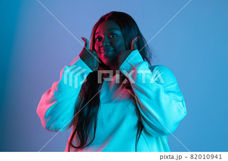 One African beautiful woman with long straight hair isolated on blue studio background in neon light. Concept of human emotions 82010941