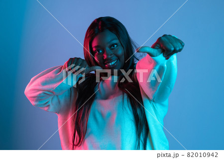 One joyful African beautiful woman with long straight hair singing isolated on blue studio background in neon light. Concept of human emotions One joyful African beautiful woman with long straight hair singing isolated on blue studio background in neon light. Concept of human emotions 82010942
