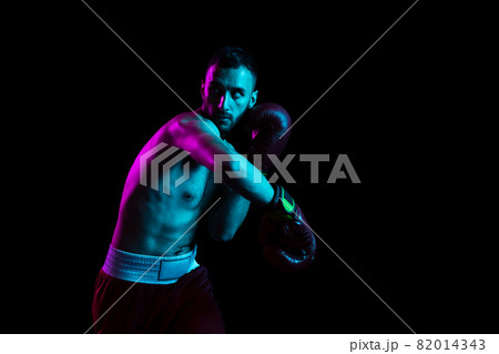 One professional male boxer training isolated over black backgrund in neon light. Knocking out the opponent One professional male boxer training isolated over black backgrund in neon light. Knocking out the opponent 82014343