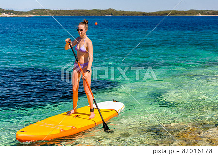 Young girl sup board with a paddle in hand - front view - the calm surface of the turquoise sea - copy space 82016178