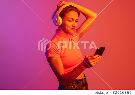 One caucasian girl in headphones putting hair up isolated over gradient background in neon lights 82016369