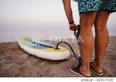 Close up of man prepares to paddle surf on a beach inflating sup board Close up of man prepares to paddle surf on a beach inflating sup board 82017536