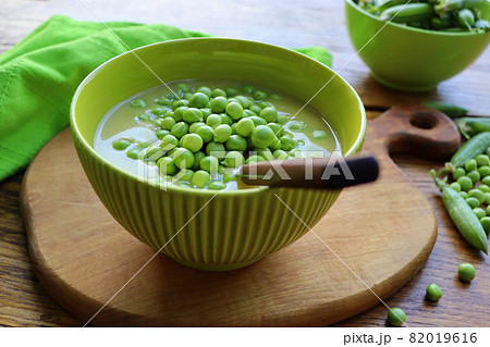 Fresh green pea soup with pea seeds and pea pods around . Selective Focus, Focus on the pea in the middle of the soup. 82019616