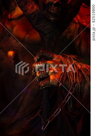 Halloween decorations, spooky creepy scary fearfull horrible terrible warlock's hand in rags with metal fingers and a chain holding frighten skull mask in bloody red orange gold colors Halloween decorations, spooky creepy scary fearfull horrible terrible warlock's hand in rags with metal fingers and a chain holding frighten skull mask in bloody red orange gold colors 82019800