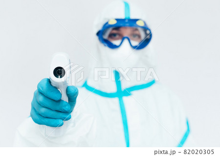 A medic in a protective medical suit and mask holds a modern infrared thermometer in his hand. 82020305