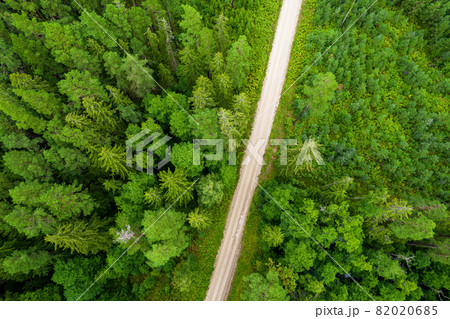 Aerial full frame view from drone of idyllic country road leading through gallant pine and birch forests in dark green colors in cloudy rainy weather  82020685
