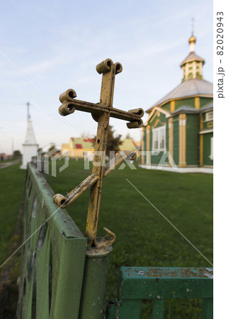 Old iron rusty Orthodox cross on an old fence. Orthodox church in the background. 82020943