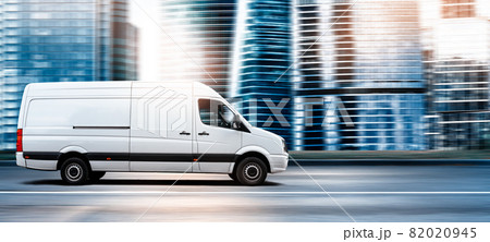 Van driving on a city road at sunset in front of a modern cityscape 82020945