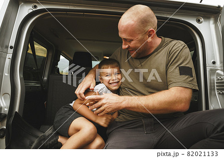 Happy father and son sitting in car trunk 82021133