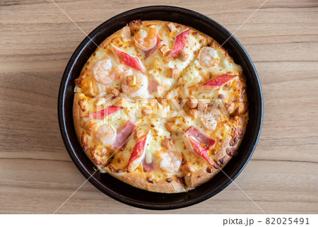 Top view of delicious seafood pizza topped with cheese, pineapple, crab sticks and shrimp on wooden table. Pizza is a favorite food for many around the world. Top view of delicious seafood pizza topped with cheese, pineapple, crab sticks and shrimp on wooden table. Pizza is a favorite food for many around the world. 82025491