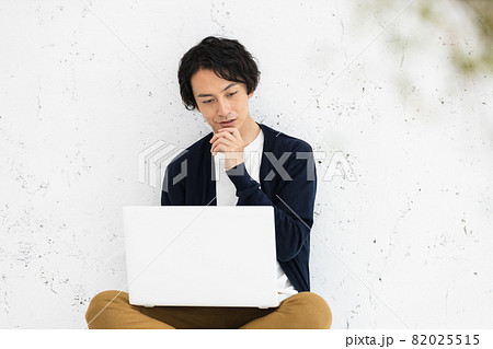 床に座ってパソコン作業をしている若い男性 床に座ってパソコン作業をしている若い男性 82025515