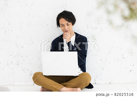 床に座ってパソコン作業をしている若い男性 床に座ってパソコン作業をしている若い男性 82025516