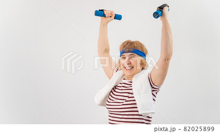 An elderly woman with a blue bandage on her head trains with dumbbells on a white background An elderly woman with a blue bandage on her head trains with dumbbells on a white background 82025899