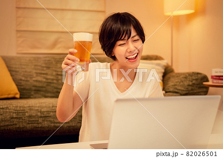 リビングでオンライン飲み会をする若い女性の写真素材