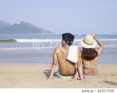young asian couple lovers sitting on beach, rear view young asian couple lovers sitting on beach, rear view 82027506