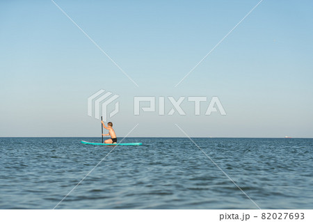A 12 year old boy learns to stand on a SUP board in the sea near the shore. 82027693