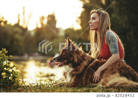 Close up of young female with her dog sitting on grass in park Close up of young female with her dog sitting on grass in park 82028452