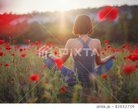 A beautiful woman meditates on a poppy field at sunset 82032730
