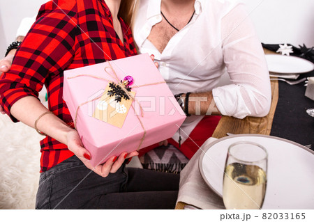 Picture showing group of friends celebrating Christmas at home and giving presents to each other. Focus on a gift in woman hands in the foreground 82033165