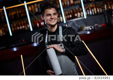 Handsome barman in apron standing at the bar counter Handsome barman in apron standing at the bar counter 82034991