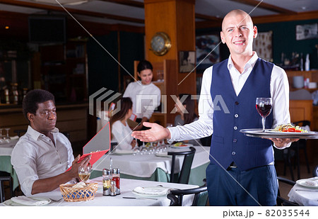 Friendly headwaiter with serving tray welcoming in restaurant 82035544