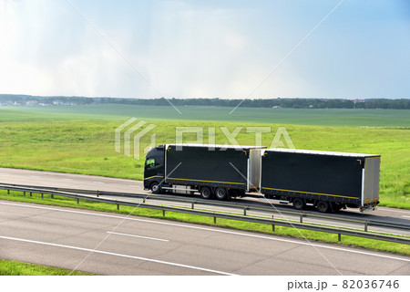 Rigid Truck and Drawbar Trailer driving along highway on the green agriculture field background.  82036746