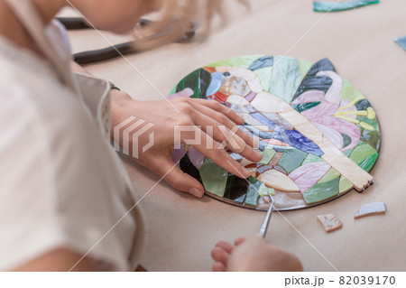 Workplace of the mosaic master: women's hands holding tool for mosaic details in the process of making a mosaic 82039170