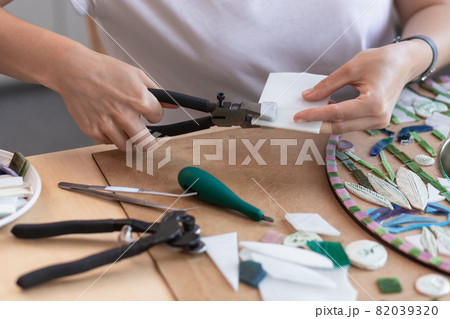 Workplace of the mosaic master: women's hands holding tool for mosaic details in the process of making a mosaic 82039320