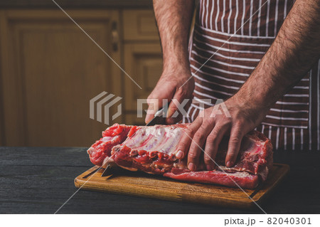 Man cuts of fresh piece of meat on a wooden cutting board in the home kitchen 82040301