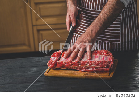 Man cuts of fresh piece of meat on a wooden cutting board in the home kitchen 82040302