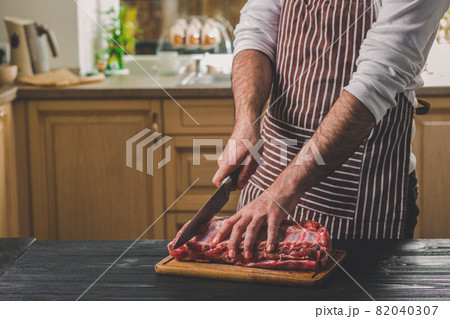 Man cuts of fresh piece of meat on a wooden cutting board in the home kitchen 82040307