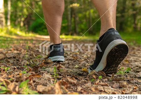 Legs in sneakers close up athlete runs in the park outdoors, around the forest, oak trees green grass young enduring athletic athlete healthy athlete forest, outdoor fit person jog, wellbeing. Autumn Legs in sneakers close up athlete runs in the park outdoors, around the forest, oak trees green grass young enduring athletic athlete healthy athlete forest, outdoor fit person jog, wellbeing. Autumn 82048998