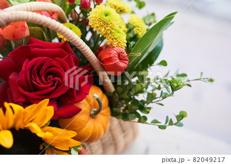 Close-up of a basket with beautiful autumn flowers made of red roses, sunflowers and green leaves. The concept of the holiday. Copy space. High quality photo 82049217