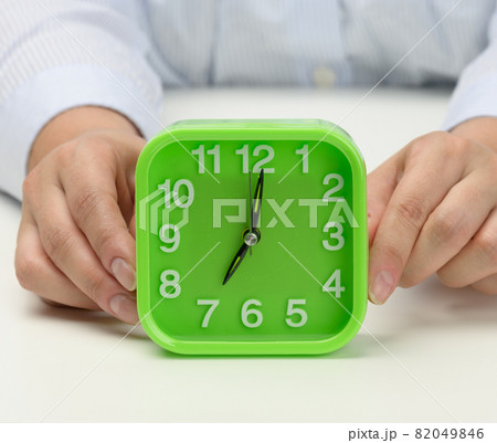 woman's hand holds a green square alarm clock, the clock shows seven in the morning. Wake up early, start the day 82049846