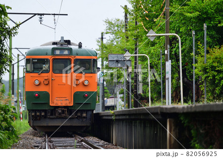 雨に濡れるローカル線の駅を出発する115系電車 82056925