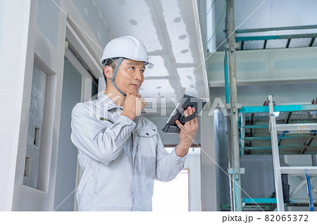 建築現場でタブレットを見ながら現場確認をする現場監督 82065372