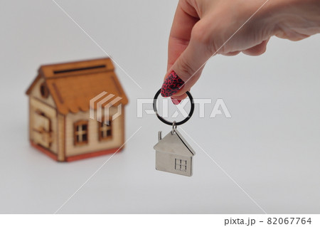 A hand holds a keychain in the shape of a house against the background of a toy deret of a withered house, mortgage, real estate purchase 82067764