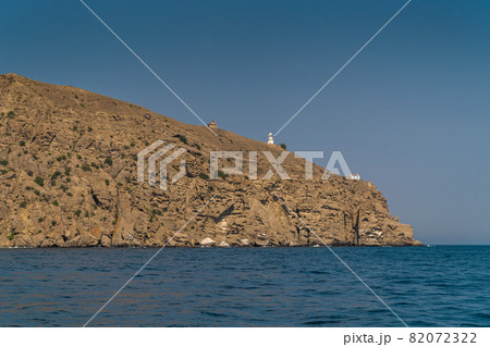The Republic of Crimea. July 21, 2021. View from the Black Sea in warm sunny weather on the lighthouse and buildings on Mount Meganom, which is located near the city of Sudak. The Republic of Crimea. July 21, 2021. View from the Black Sea in warm sunny weather on the lighthouse and buildings on Mount Meganom, which is located near the city of Sudak. 82072322
