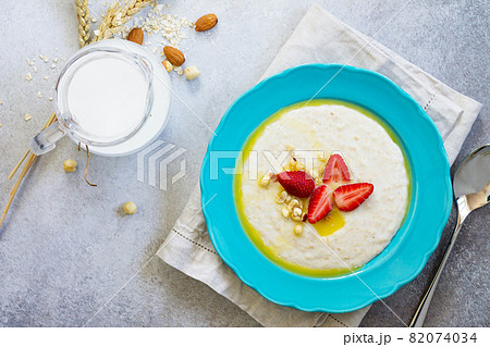 Healthy breakfast. Porridge of oatmeal with nuts, milk and fresh strawberries on stone or slate background. The concept of nutrition health. Copy space, top view flat lay background. 82074034
