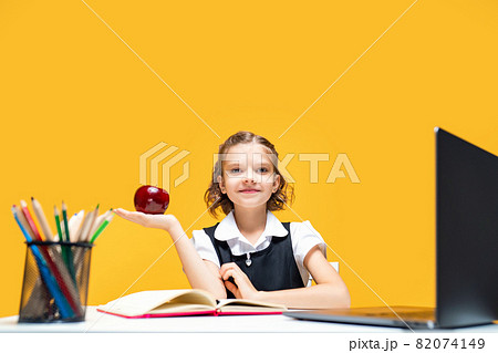 Little schoolgirl holding an apple in hand while change at online lesson. Distance education Little schoolgirl holding an apple in hand while change at online lesson. Distance education 82074149