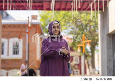 Islamic beautiful woman in a Muslim dress standing on a summer park street background forest autumn trees.world hijab day. Islamic beautiful woman in a Muslim dress standing on a summer park street background forest autumn trees.world hijab day. 82076360