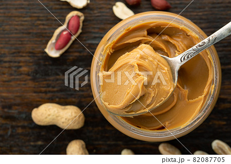 Peanut butter in an open jar and heap of nuts on wood background. Peanut butter in an open jar and heap of nuts on wood background. 82087705