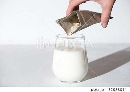 hand holding collagen powder travel pack and adding it to a milk to make protein cocktail. collagen peptides powder for healthy milkshake. joints care. 82088014